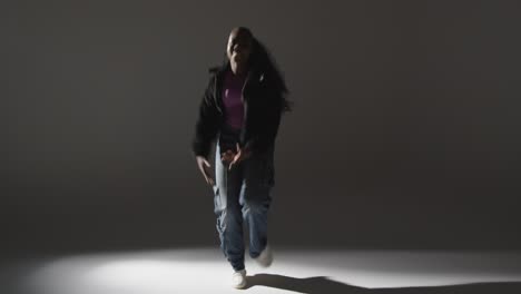 full length studio portrait shot of young woman dancing with low key lighting against grey background 4