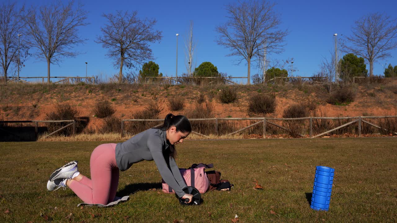 joven mujer caucásica en forma haciendo ejercicios de músculos abdominales con rueda de rodillos abdominales en el parque