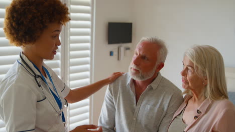 female nurse wearing uniform giving senior couple good news in private hospital room