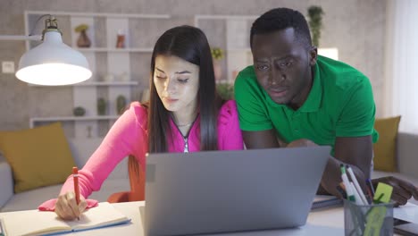 Multiethnic couple working in home office using laptop, taking notes and doing brainstorming.