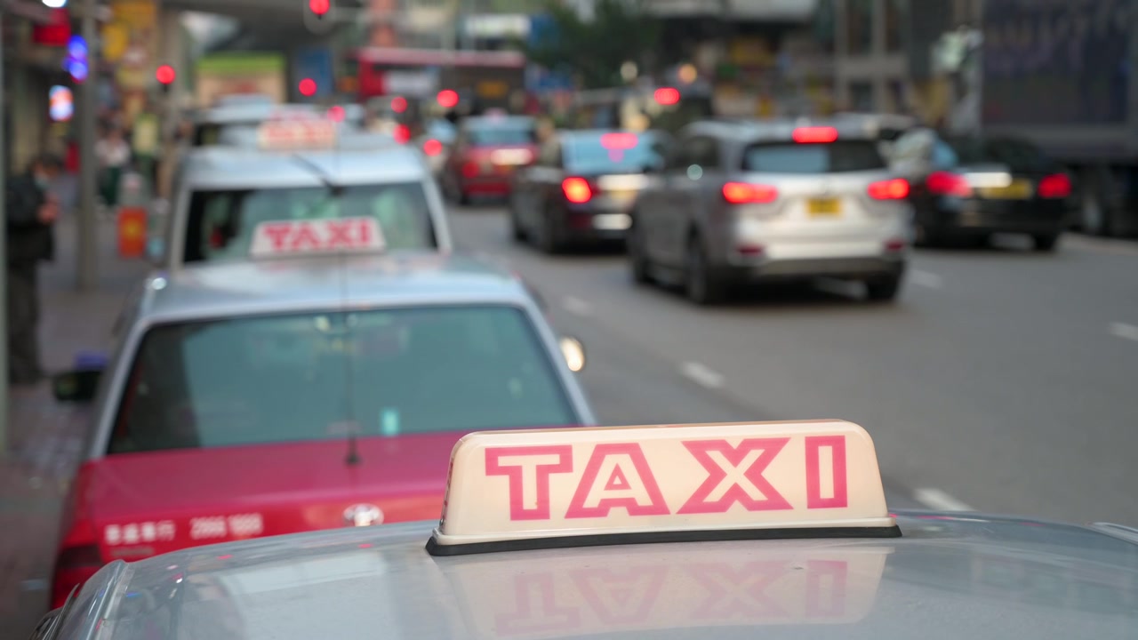 En kø af taxaer med oplyste skilte på motorhjelmen, set parkeret i vejkanten, venter på kunder.