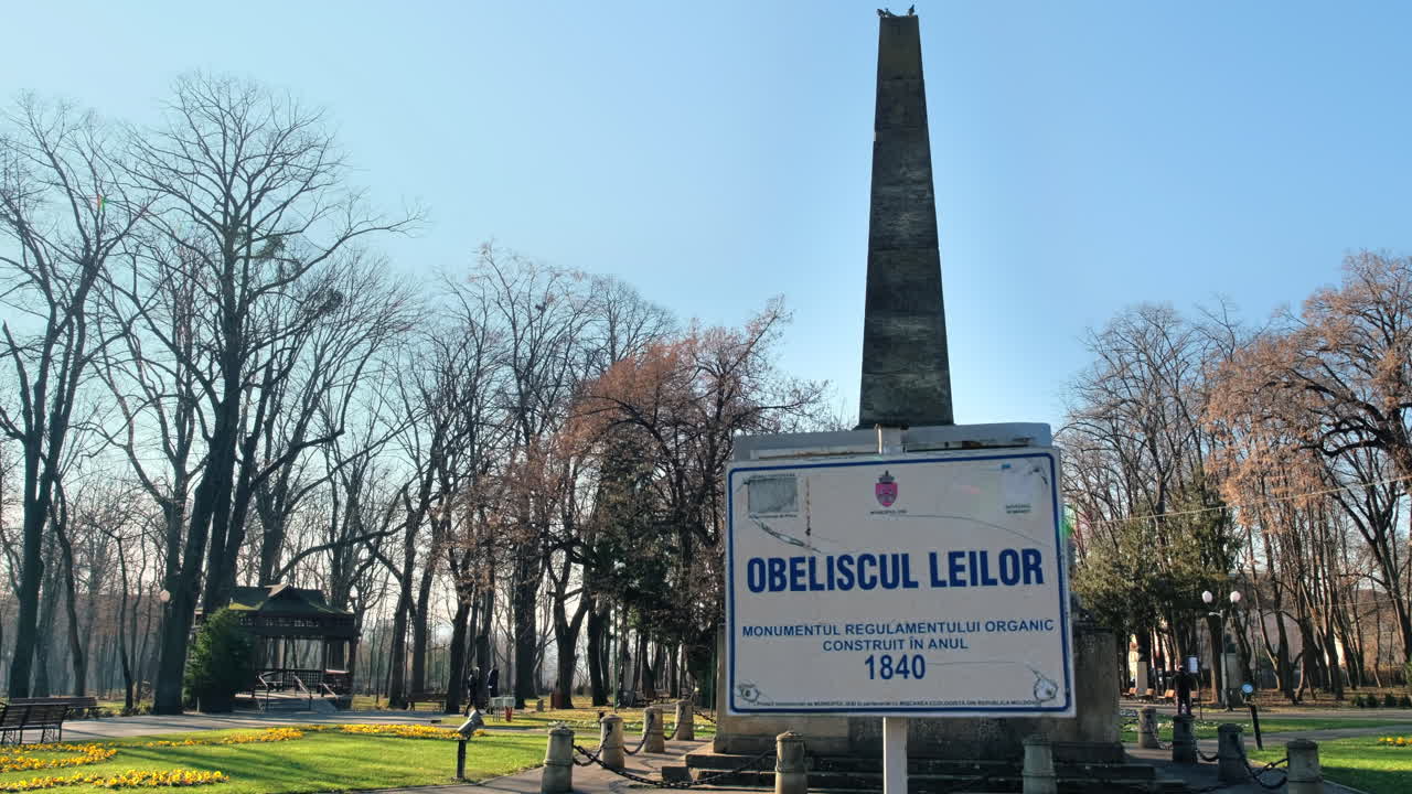 View of Copou Park in Iasi, Romania. Lions Obelisk, alleys, bare trees, green grass and flower beds, people