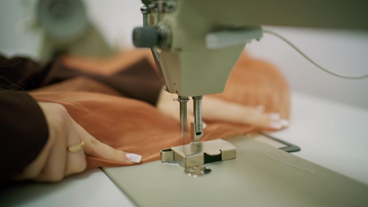 Close up of a person guiding brown sheer fabric under the needle of an industrial sewing machine