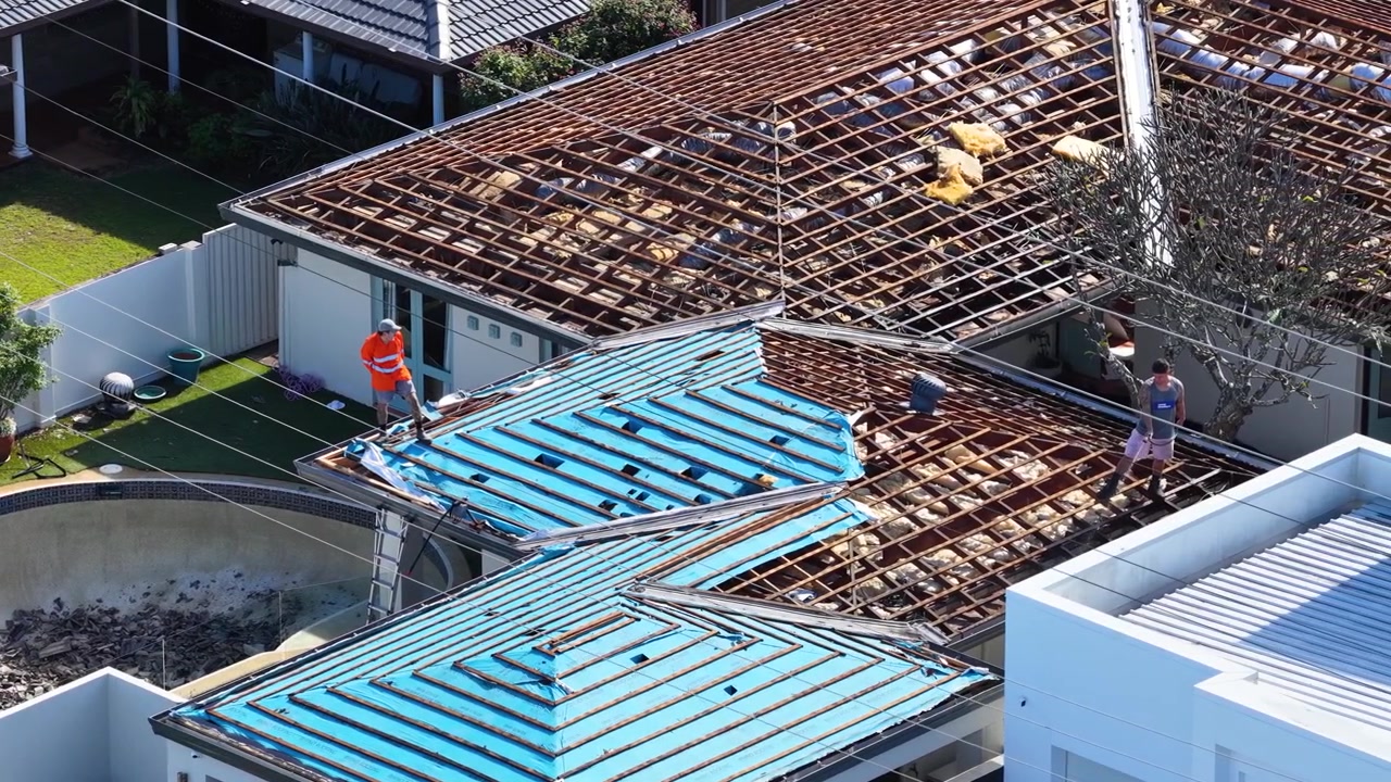 Aerial view of workers in high-visibility vests repairing a suburban house roof under bright sunlight.