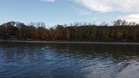 drone footage of a caucasian woman paddling a blue kayak over buffalo lake on a cloudy autumn day