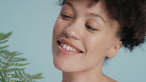 close up portrait beautiful mixed race woman touching face with fern leaf caressing smooth healthy skin complexion enjoying playful natural beauty on blue background skincare concept