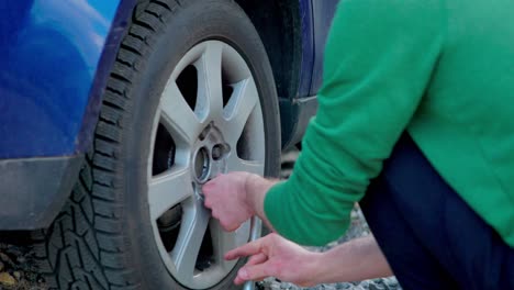 person spins lug wrench around lug nuts taking them off to replace flat tire on side of road