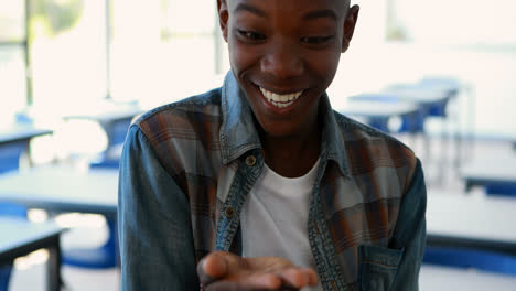 Happy-schoolboy-looking-at-hand-in-classroom