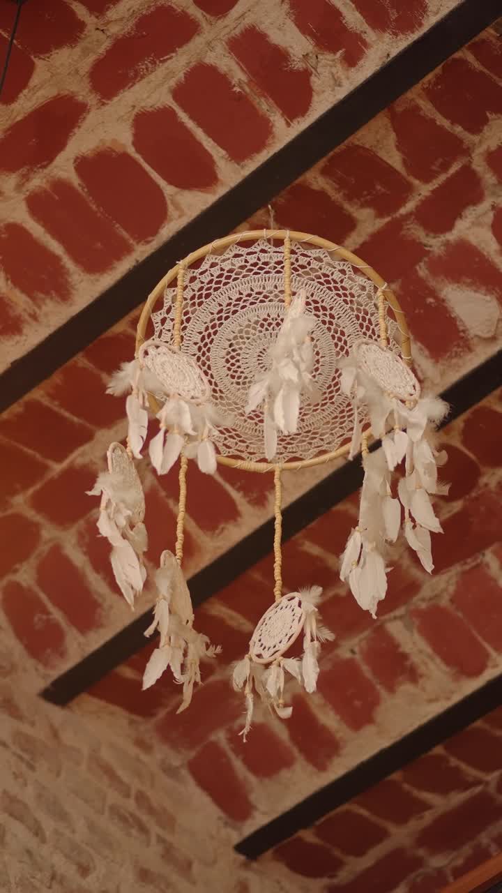Acchiappasogni bianco con piume appeso a un soffitto rustico in mattoni.