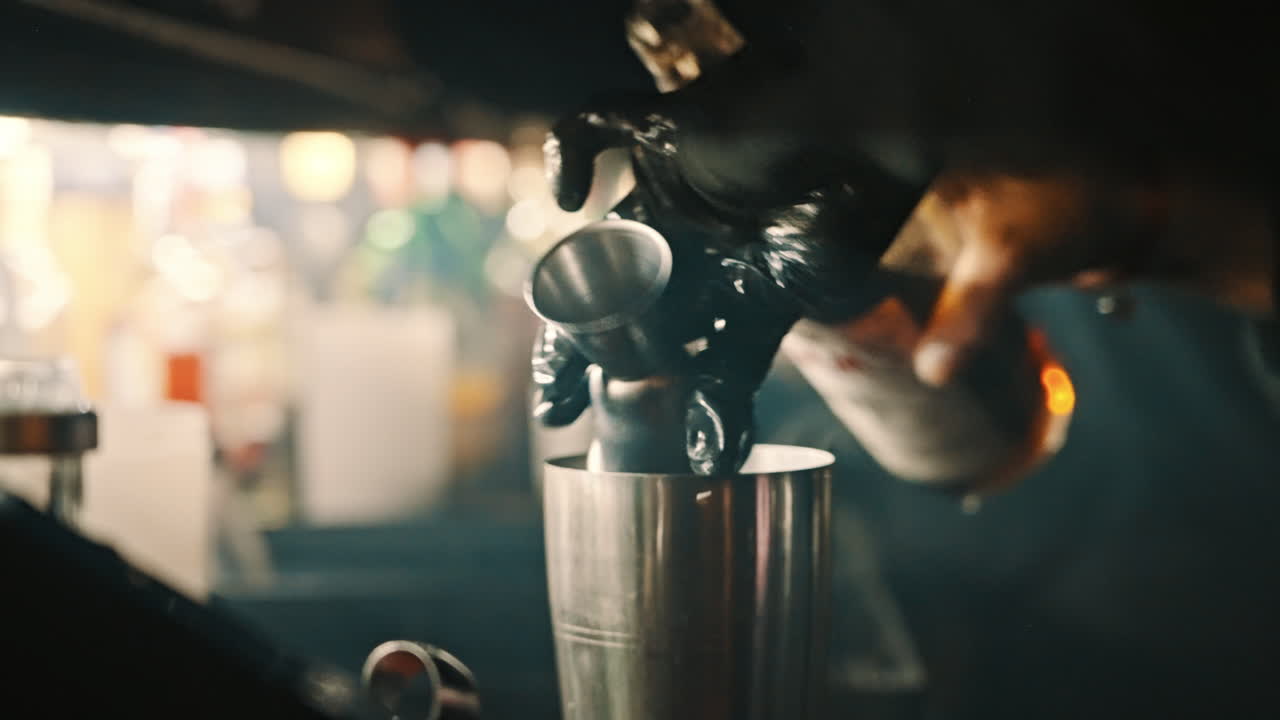 Mani di un barista che versano liquido da un jigger in uno shaker per cocktail