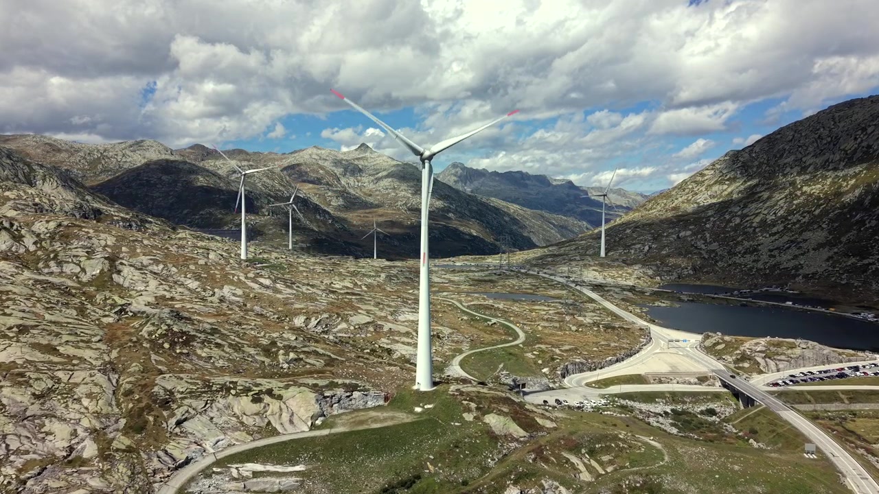 Dolly aéreo para frente passando por turbina eólica em paisagem rochosa dos Alpes suíços