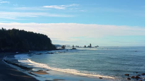 Stunning-aerial-drone-rising-shot-of-the-gorgeous-Third-Beach-in-Forks,-Washington-with-large-rock-formations,-surrounded-by-a-pine-tree-forest-on-cliffs,-and-golden-sand-on-a-warm-summer-morning