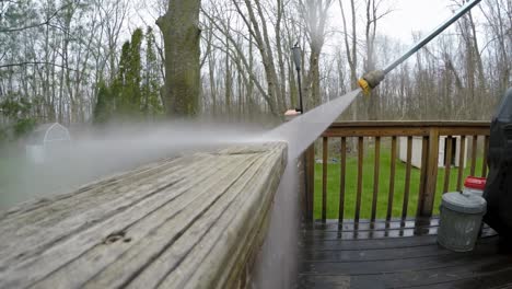 a man uses a power washer to clean a wooden deck railing post