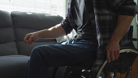 caucasian disabled man in wheelchair sitting on sofa in living room