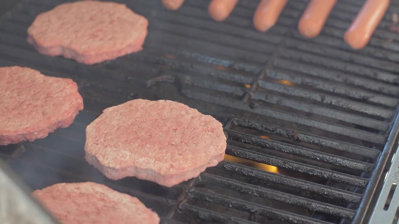 Placing Frozen Burgers on a Flaming Grill, Close Up