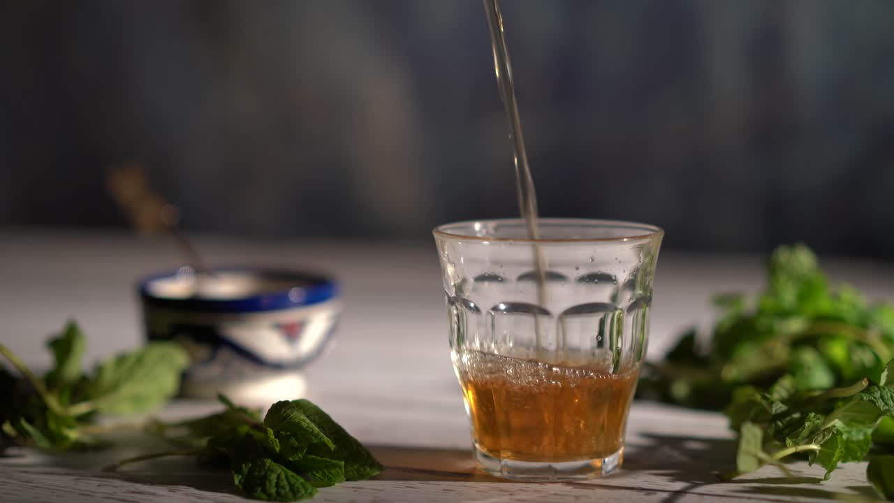 화려한 찻주전자를 들고 모로코 그릇과 민트가 있는 유리잔에 차를 붓는 넓은 손