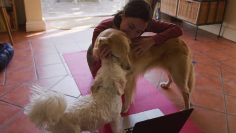 Caucasian-woman-exercising-and-stroking-her-pet-dogs-using-laptop-at-home