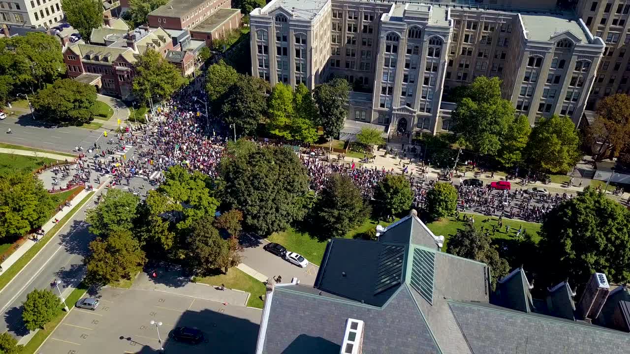 Huge crowd marches past old buildings in Toronto, aerial drone pan