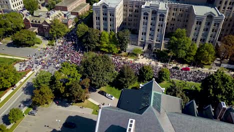 Huge crowd marches past old buildings in Toronto, aerial drone pan