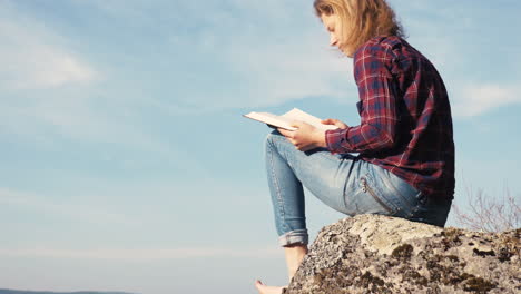 girl reading and flipping pages in the bible on a rock at a lake