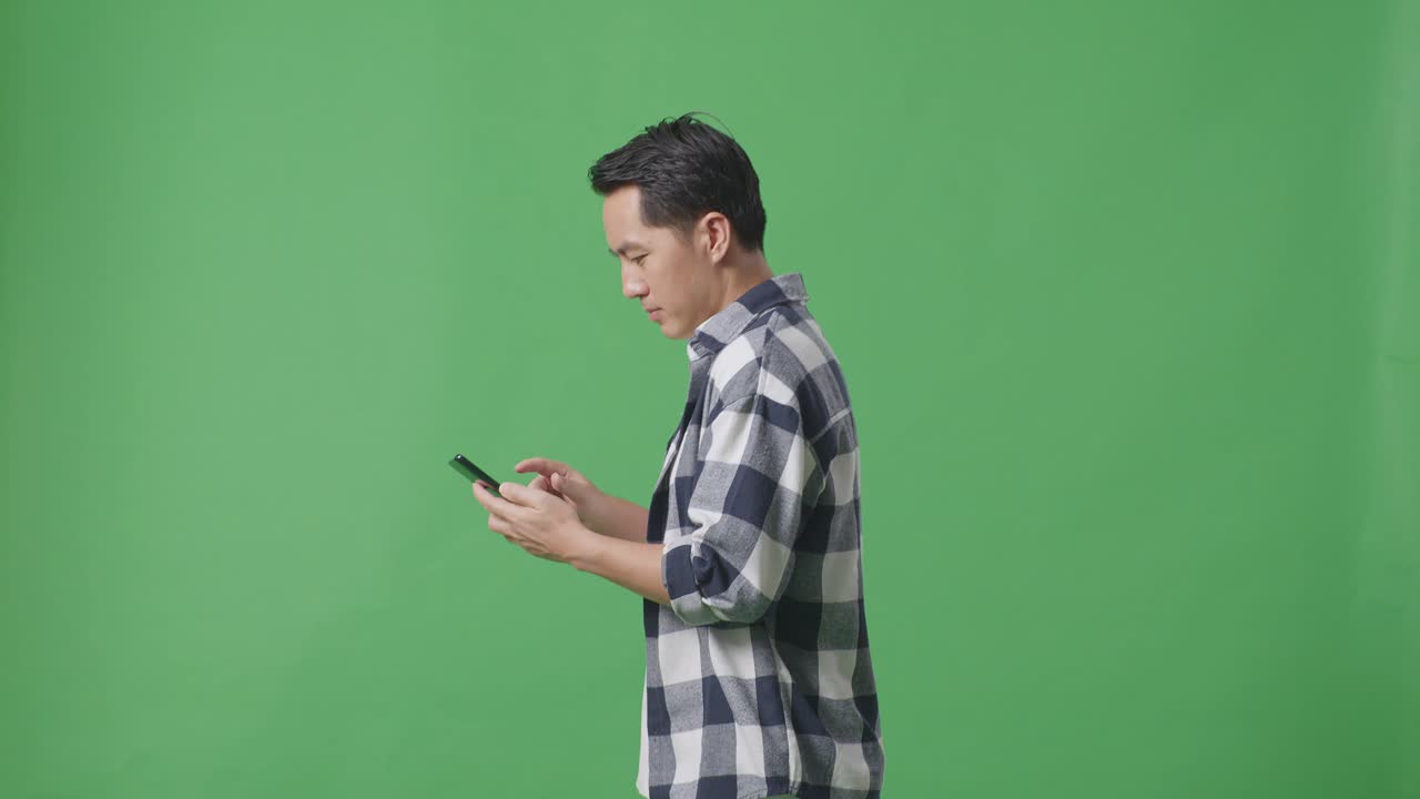 스튜디오에서 녹색 화면에서 는 동안 휴대 전화를 사용하는 아시아 남자의 측면 시각