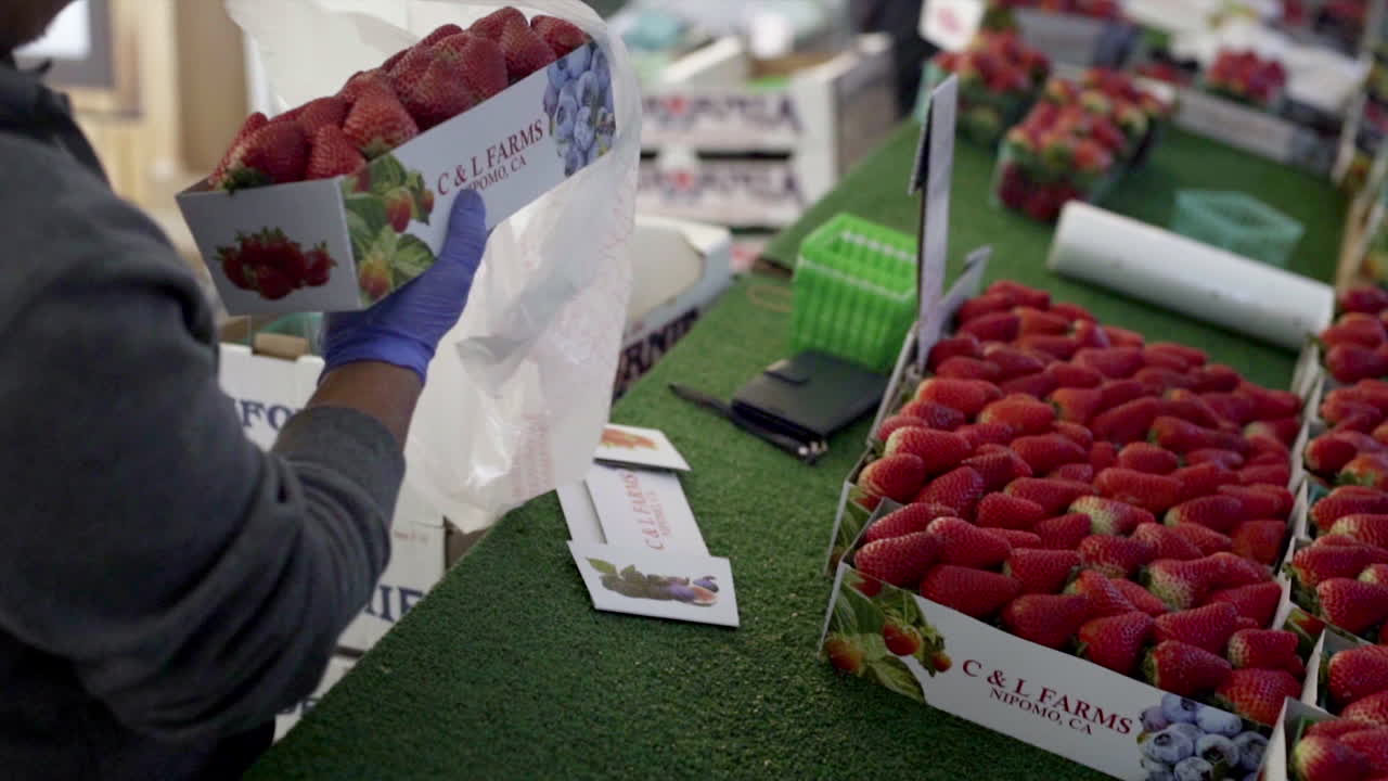 Person preparing or buying strawberries in a bag at a fresh produce market