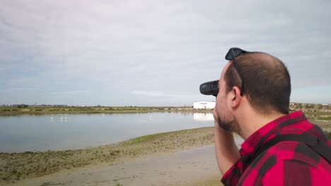 man bird watching flamingos with binoculars, over the shoulder closeup