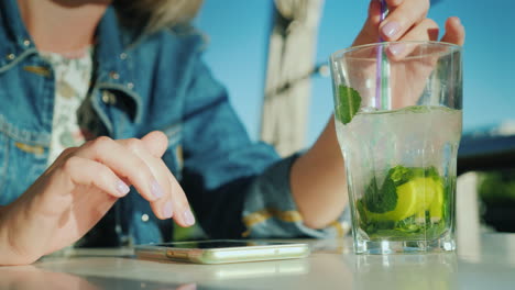 a woman is using a smartphone in a cafe there is a glass with a cocktail beside her to rest and busi