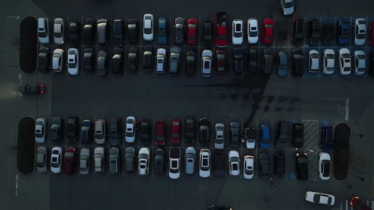 Ripresa aerea dall'alto di un parcheggio buio pieno di auto e trafficato con veicoli che entrano ed escono dagli stalli
