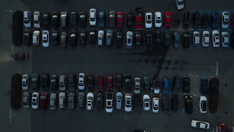 Toma-Aérea-De-Arriba-Hacia-Abajo-De-Un-Estacionamiento-Oscuro-Lleno-De-Autos-Y-Ocupado-Con-Autos-Que-Entran-Y-Salen-De-Los-Lugares-De-Estacionamiento