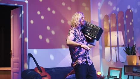 young stylish caucasian man with long hair holding boom box and dancing energetically in a retro party at home