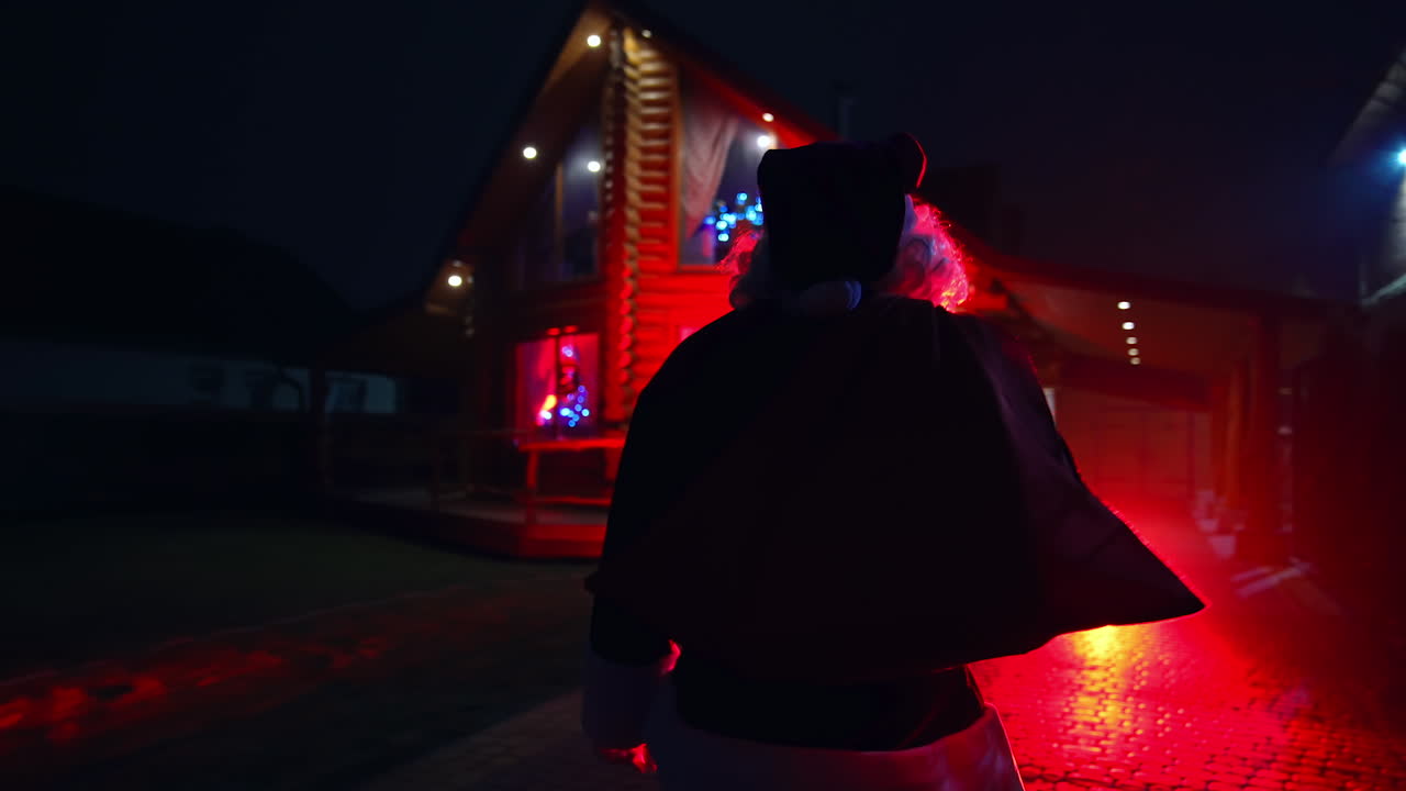 Santa Claus walking on pavement. Father Frost at Christmas outdoors. Santa walking on a pavement at dark. Red lighting. Back view