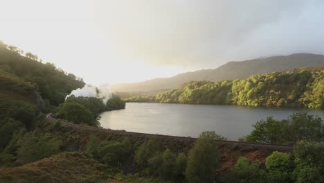 Jacobite-Steam-Train-passing-loch-on-West-Highland-Line-between-Mallaig-and-Fort-William,-Highlands,-Scotland