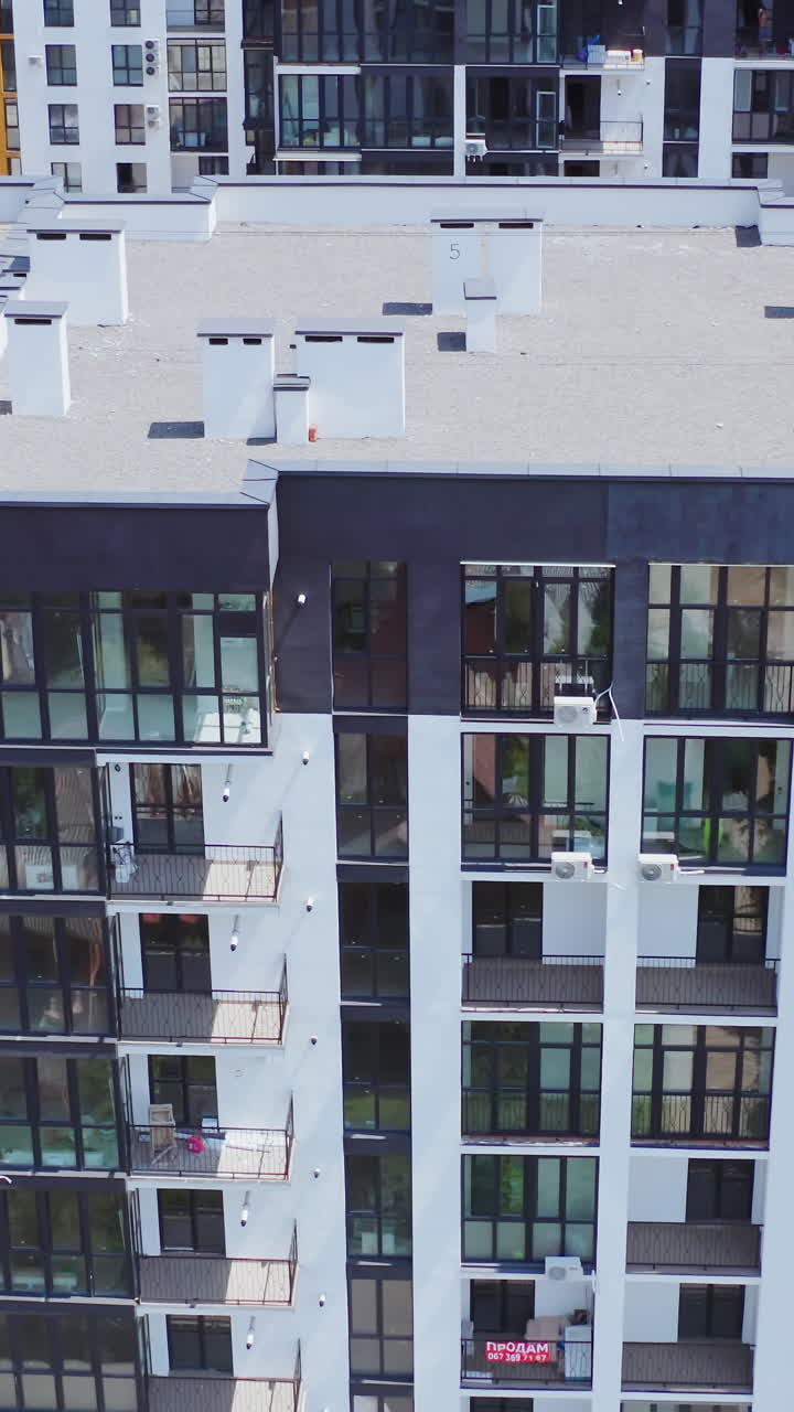 New house for city residents. Contemporary apartment building with large windows and beautiful walls of the facade. City landscape reflects in the windows of a high-raised building. Aerial view. Vertical video