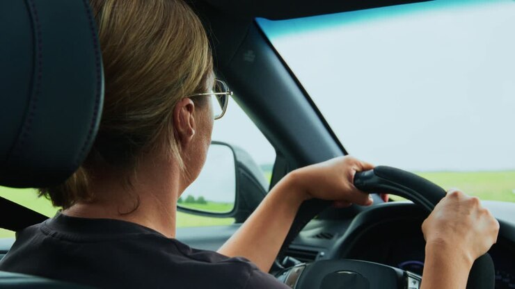 Donna alla guida di un'auto in viaggio attraverso campi verdi