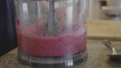 closeup of a person is using a blender to mix raspberries in a kitchen