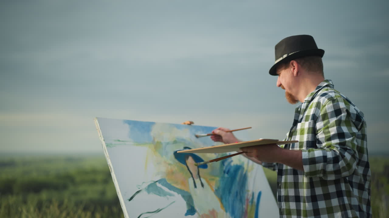 An artist wearing a black hat and a checkered shirt is seen painting on a canvas, holding a palette in a serene grassy environment. A blurred bird is visible flying across the sky