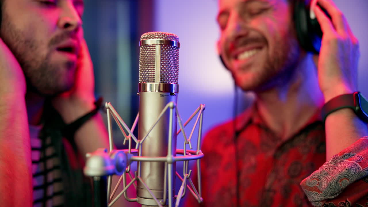 Two men singing into a microphone in a recording studio