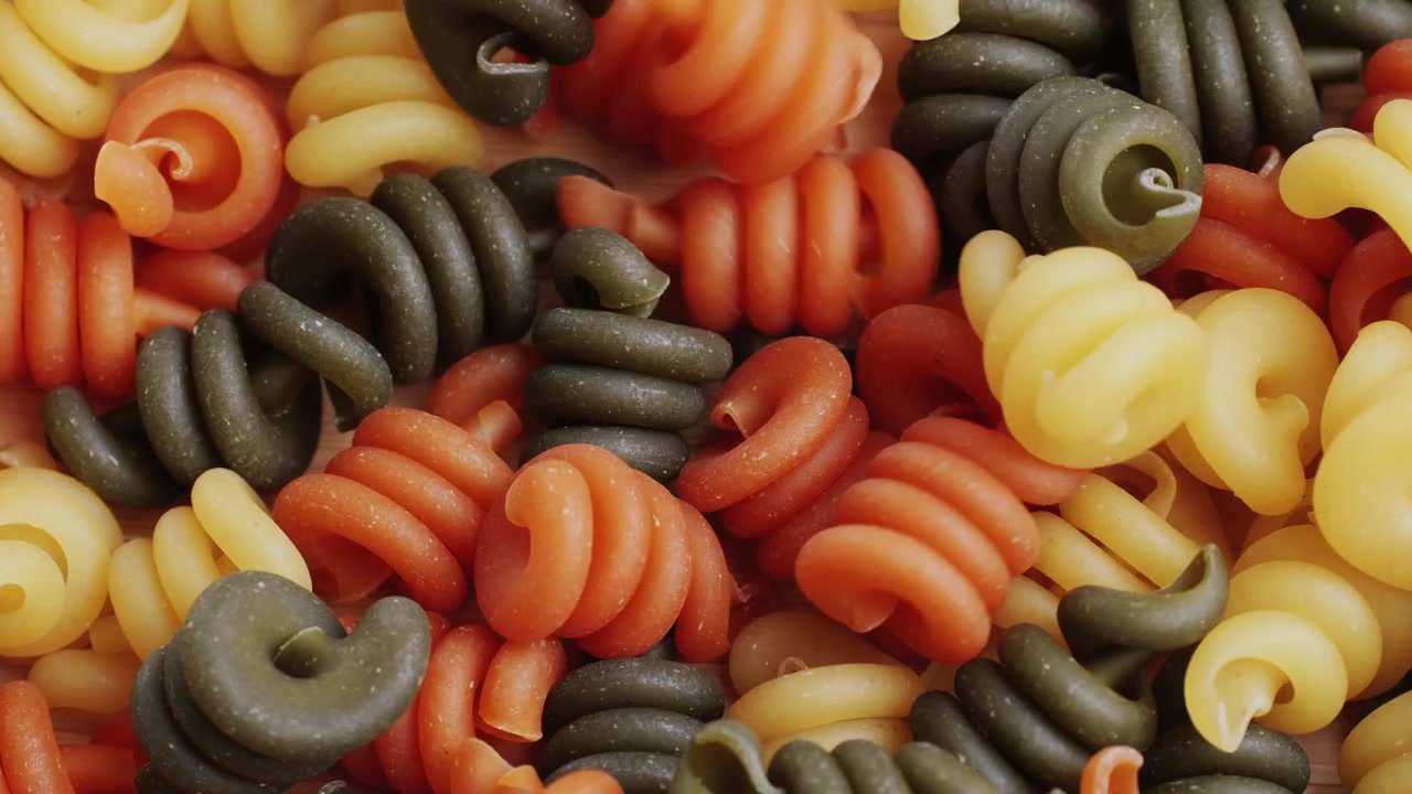 Close-Up of Colorful Spiral Pasta Falling onto a Wooden Surface