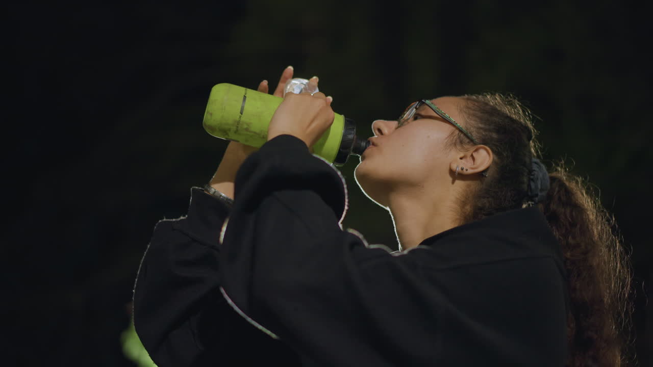 Green Bottle Ritual For Training Session Start, Focused Athlete Gets Reusable Bottle Ready For Evening Workout, Preexercise Routine Involves Packing And Focusing On Hydration Tools For Event