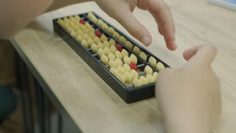 a black abacus with a red bead rests on a wooden table.