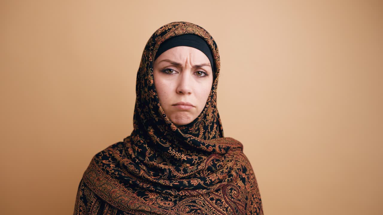 Upset Muslim Woman Wearing Hijab Looks at Camera with Frowning Expression