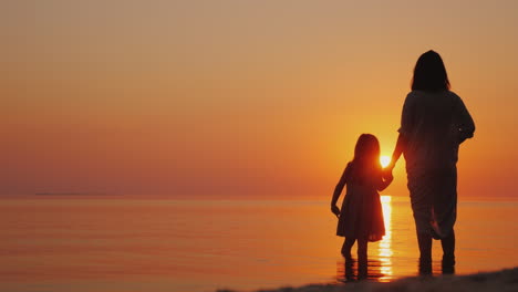 silhouette of a pregnant woman with a baby near by stand near the sea at sunset waiting for the seco