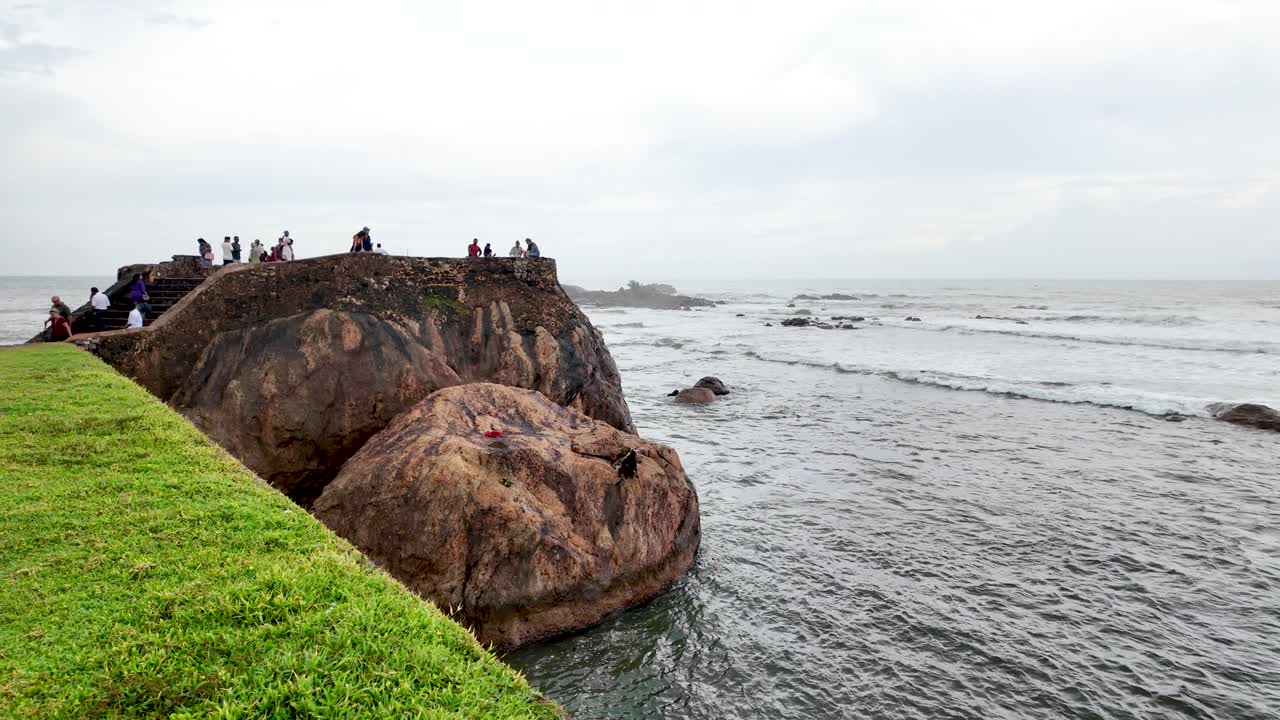 View of Flagrock Bastion along the coastline in Galle, Sri Lanka, with people enjoying the seaside scenery. Captures the beauty of nature and historical architecture.