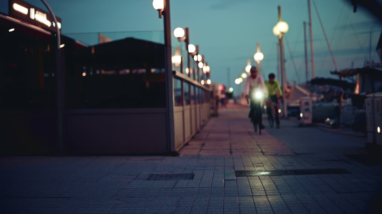Cannes, France - November 8, 2025: Nighttime scene of a cyclist with a bright headlight riding along a marina walkway lined with glowing lamps and passing pedestrians