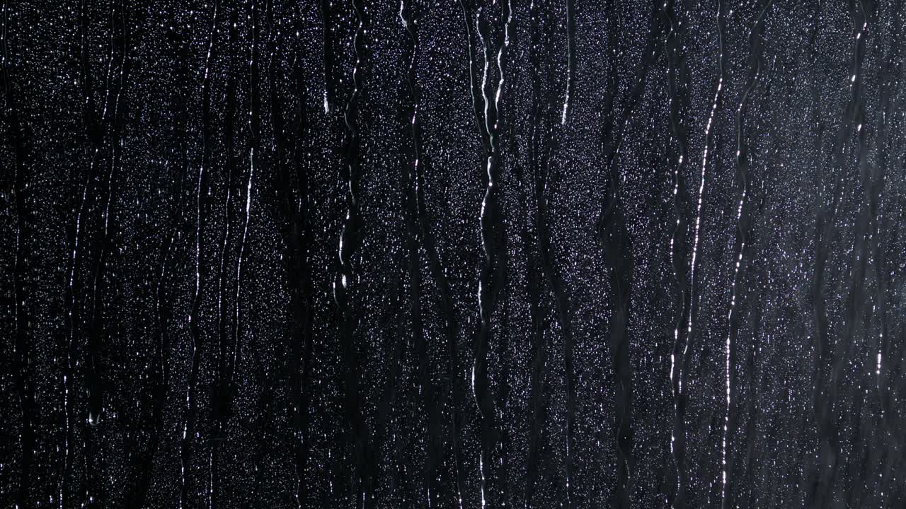 Droplets of water on black glass running down