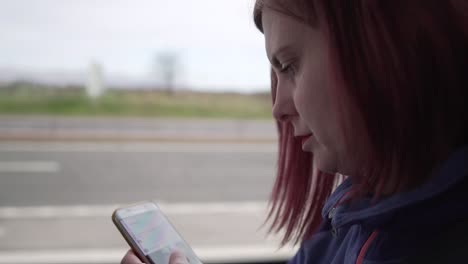 Slow-motion-close-up-shot-of-a-girl-browsing-her-smartphone-while-driving-in-a-vehicle-with-motion-in-the-background