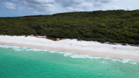 A-4k-drone-video-that-flies-backwards-to-reveal-more-of-a-beautiful-white-sand-beach-with-a-bright-blue-ocean-as-the-waves-roll-calmly-against-the-shore