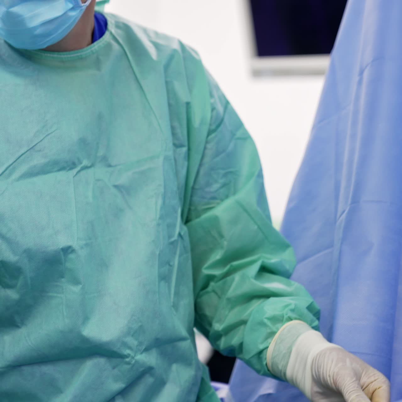 Adult male surgeon dressed for operation stands near the patient. Doctor takes a syringe and attaches it to the needle input into patient's belly