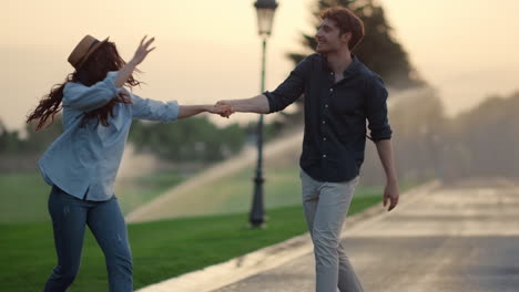 strong man taking woman on hands on road. girl and guy spinning around in park